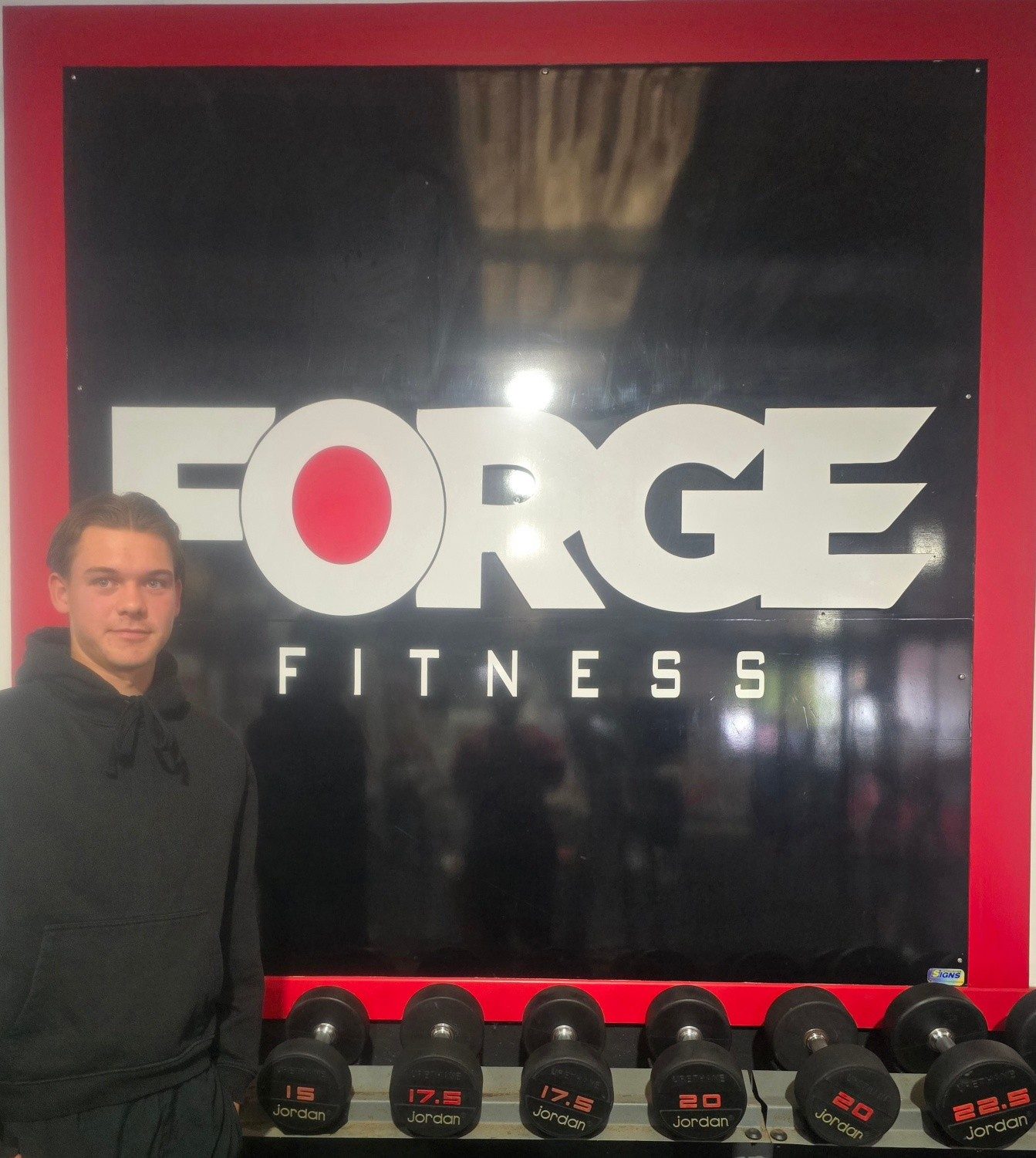 Outside Forge Fitness, in front of the FORGE sign and a dumbbell rack